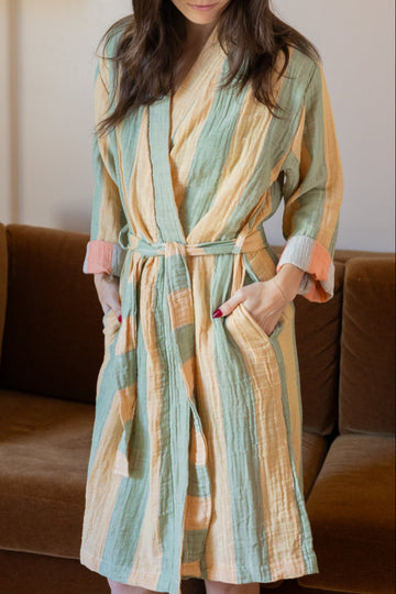 Woman wearing a striped robe in a room with a brown couch and lamp.