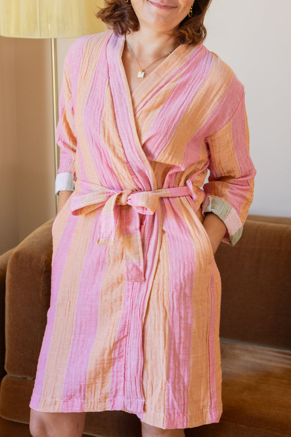 Woman wearing a pink robe sitting on a couch in a room with a lamp.
