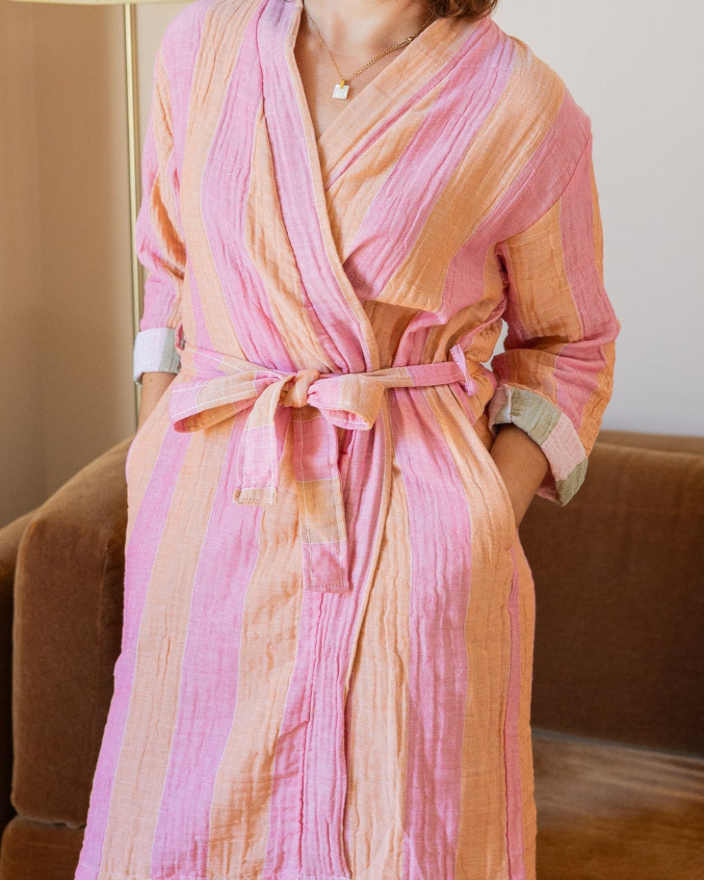 Woman wearing a pink robe sitting on a couch in a room with a lamp.