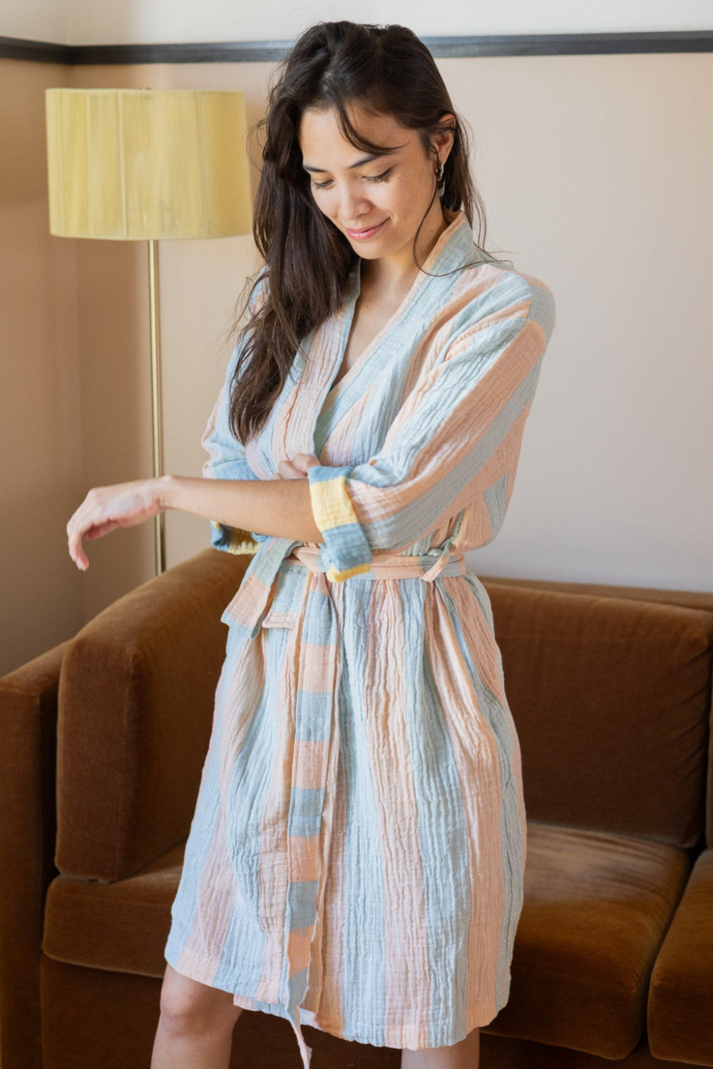 Woman wearing a patterned robe standing in a room with a brown couch and lamp.