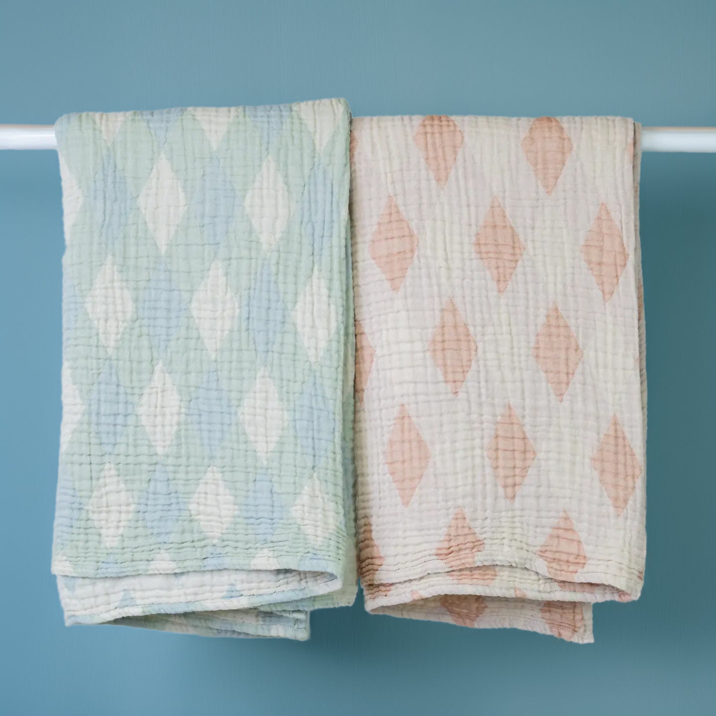 Two patterned baby blankets hanging on a rack against a blue background