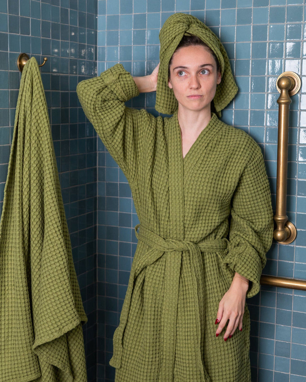 Woman wearing a green checkered robe and towel in a bathroom with blue tiles.