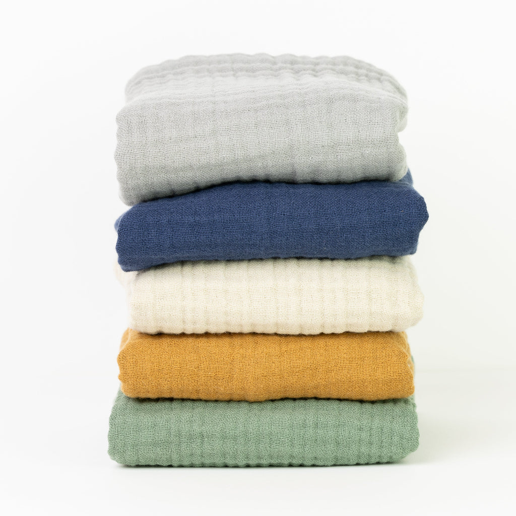 A stack of folded hand and face towels in various colors including blue, white, yellow, and green, made from gauze fabric.