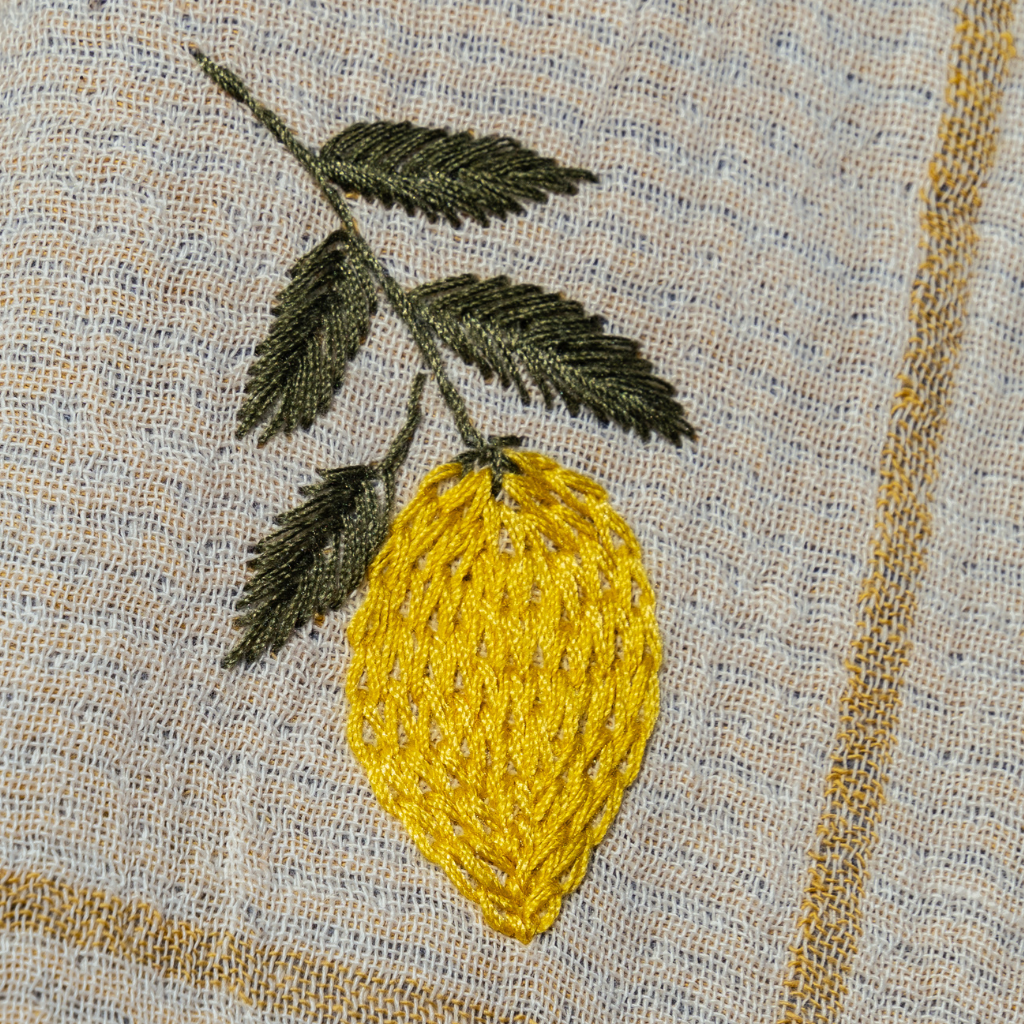 Embroidered yellow lemon with green leaves on a textured fabric background