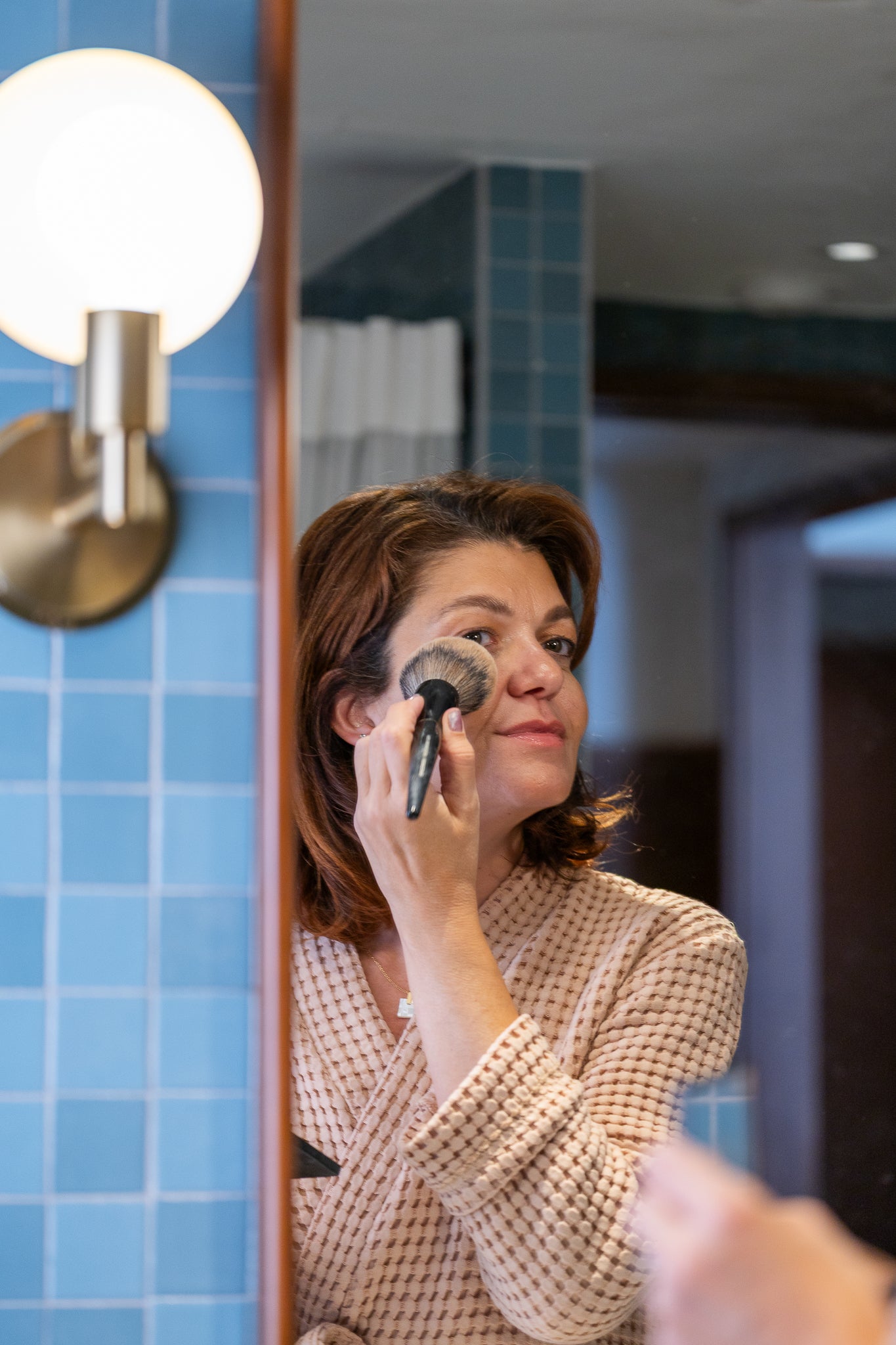 Woman wearing a sienna waffle robe applying makeup in front of a bathroom mirror