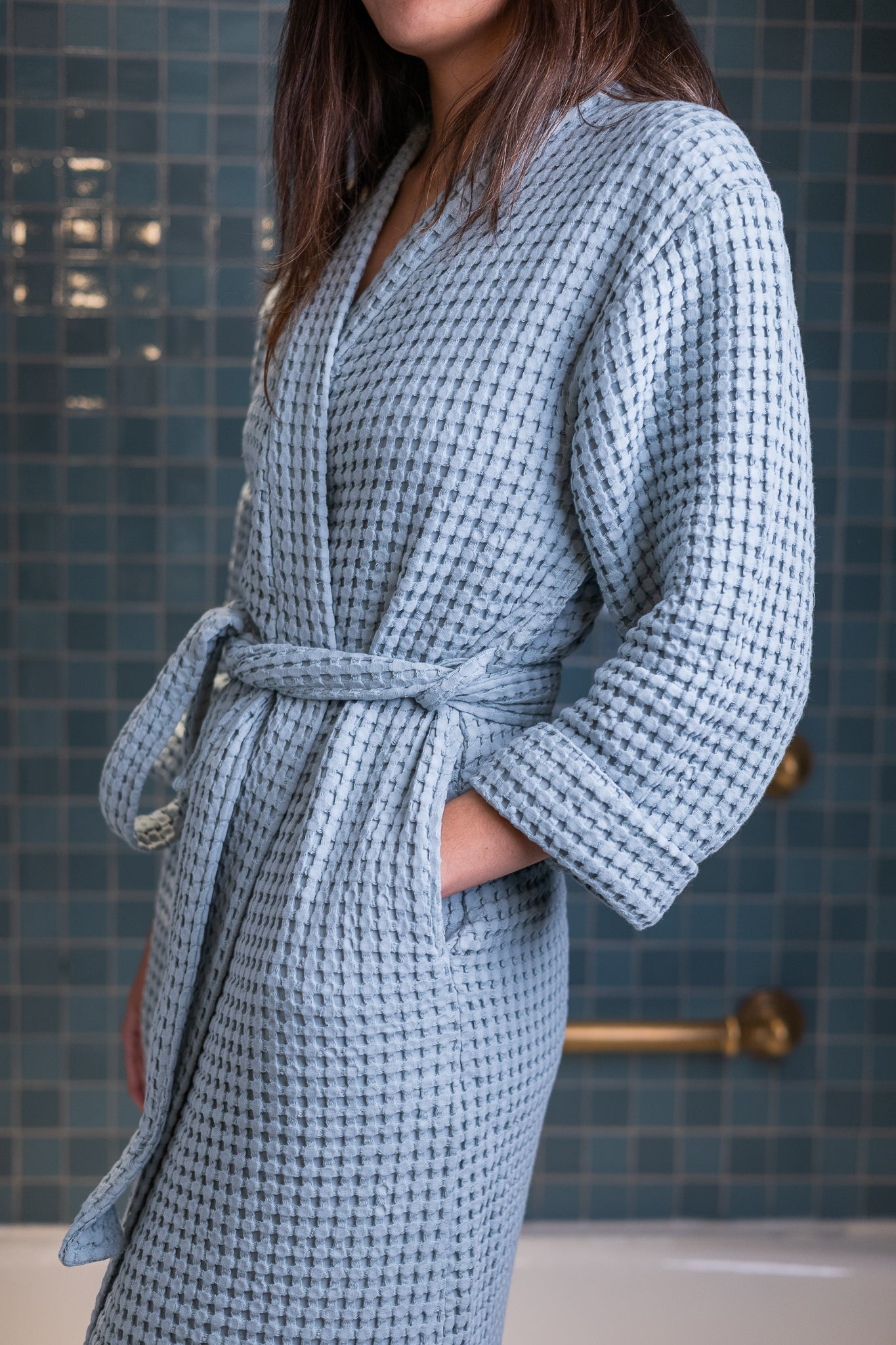 Woman wearing a sky blue waffle robe in a bathroom setting.