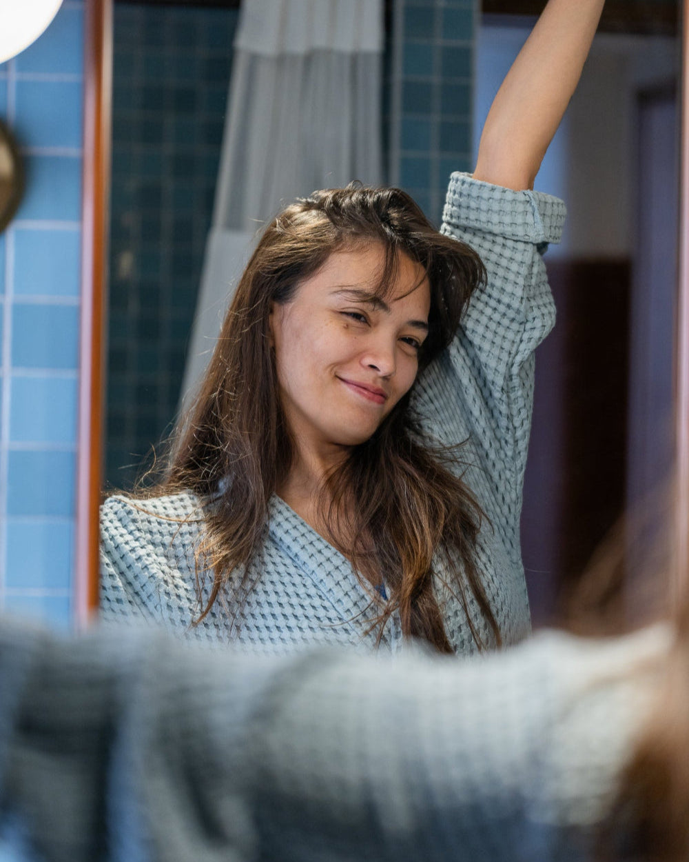 Woman stretching in front of a mirror and blue tiles wearing a blue waffle bathroom.