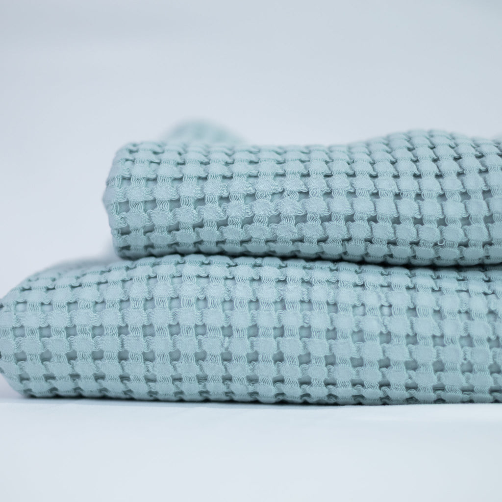 Two folded textured blue towels on a light grey background