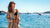 Woman by the water wearing sunglasses and a striped cover-up with boats in the background.