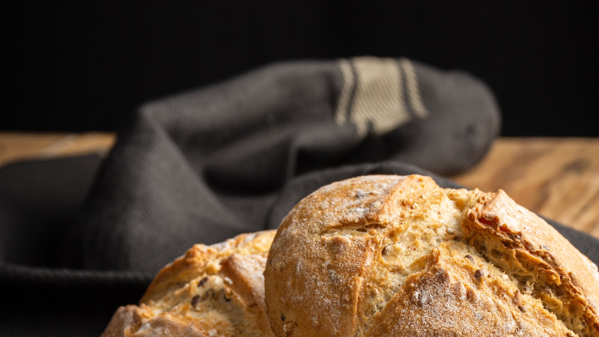 Loaf of bread on a wooden surface with a dark napkin in the background