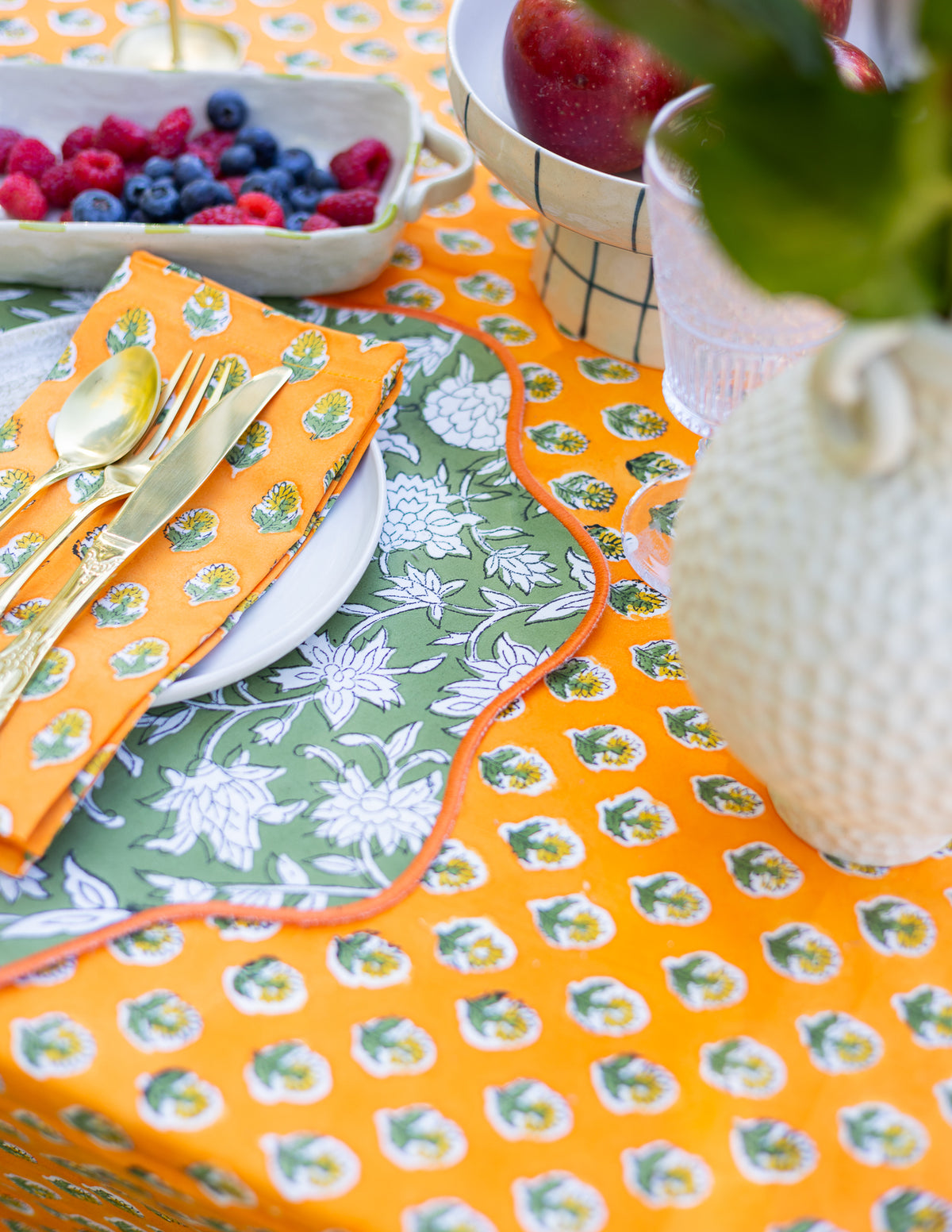 Colorful table setting with patterned placemats, cutlery, and fruit bowl.