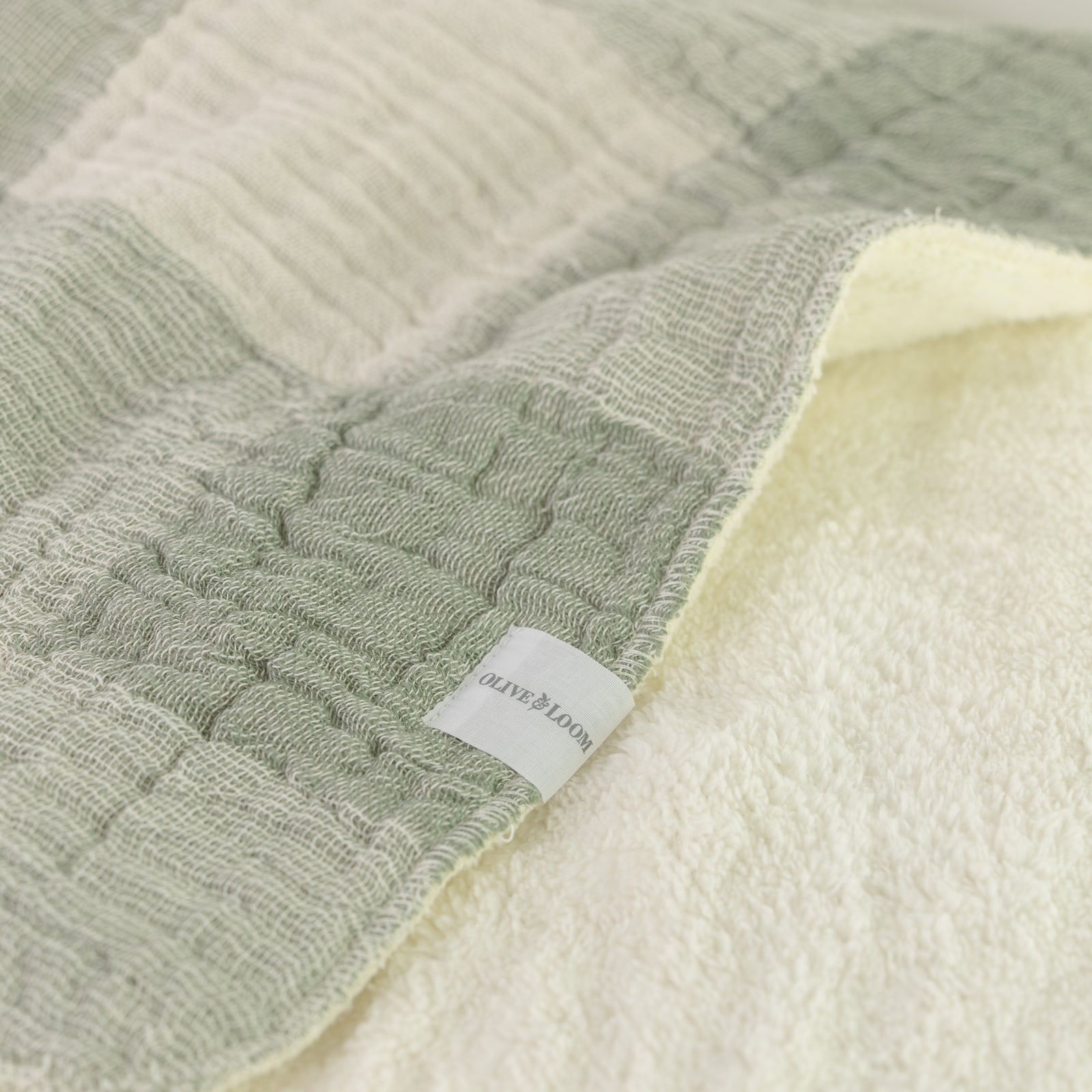 Close-up of a green and white muslin throw blanket with a soft, plush texture, made from Turkish cotton.