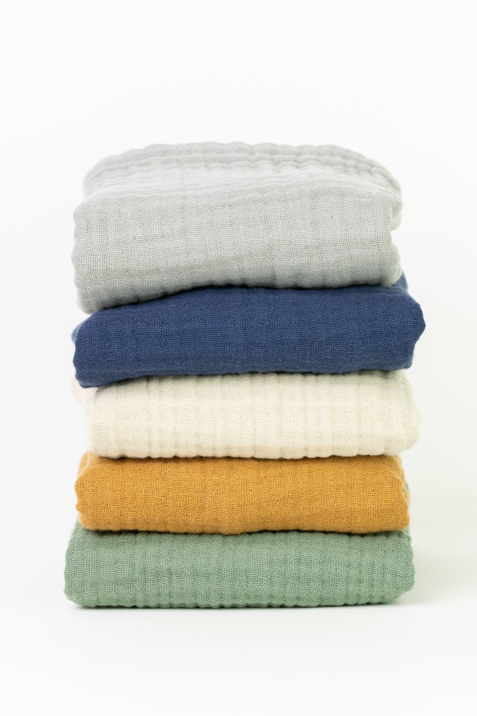 A stack of folded hand and face towels in various colors including blue, white, yellow, and green, neatly arranged on a neutral background.