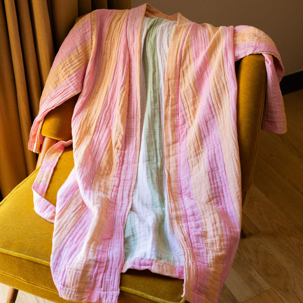 Pastel striped bath robe draped over a yellow chair against a neutral wall.