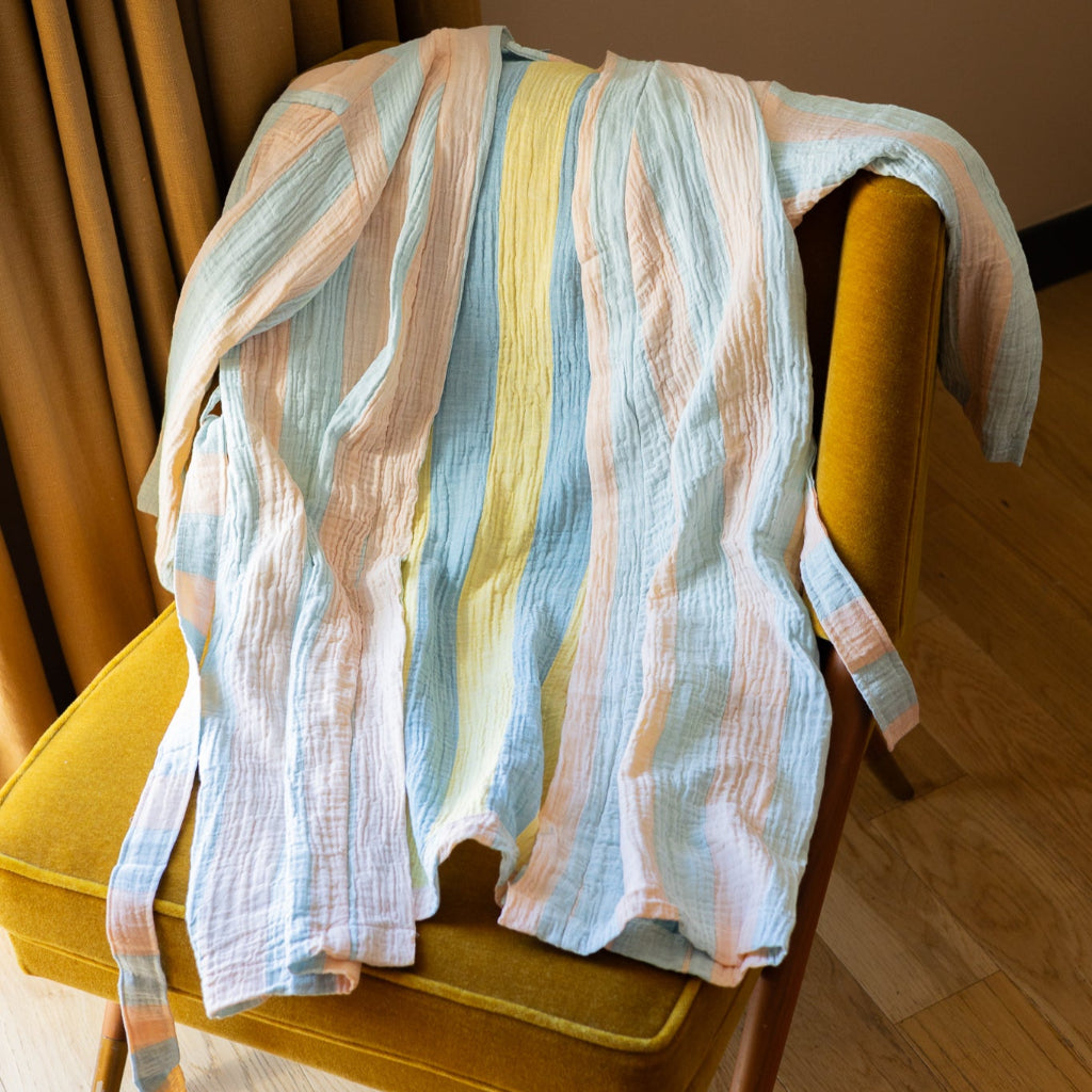 Pastel striped garment draped over a yellow chair against a neutral wall.