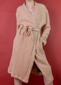 Woman wearing a sienna beige waffle robe against a red background
