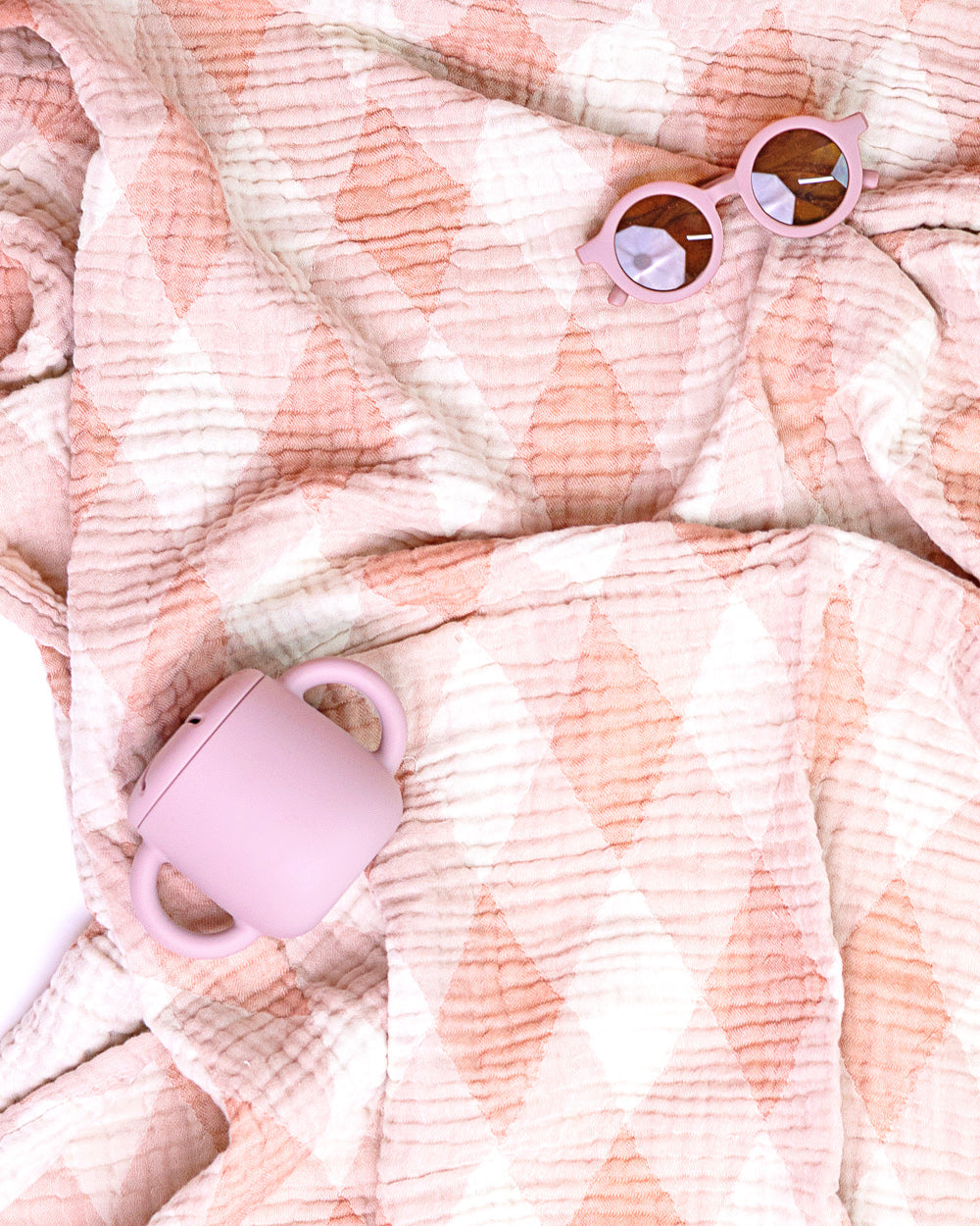 Pink sunglasses and toddler sippy cup on a textured pink blanket