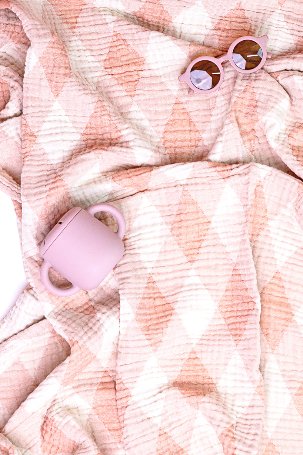 Pink sunglasses and toddler sippy cup on a textured pink blanket