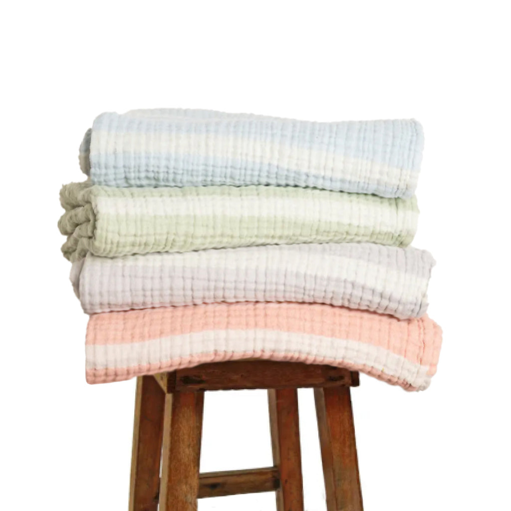 Stack of colorful baby blankets on a wooden stool against a white background