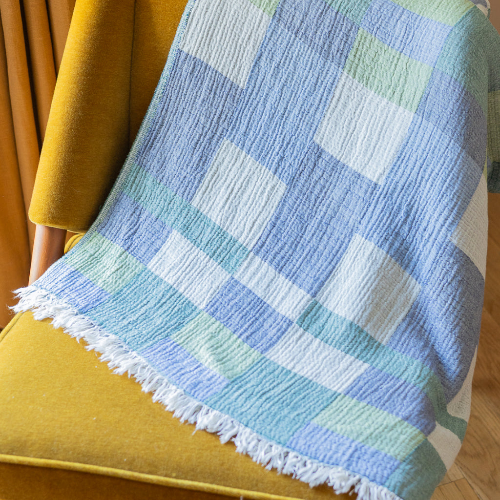 Plaid blanket with fringes draped over a blue chair next to sheer curtains.