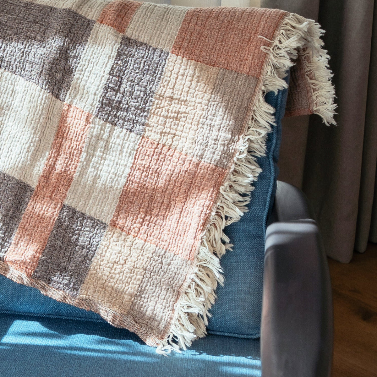 Plaid blanket with fringes draped over a blue chair next to sheer curtains.