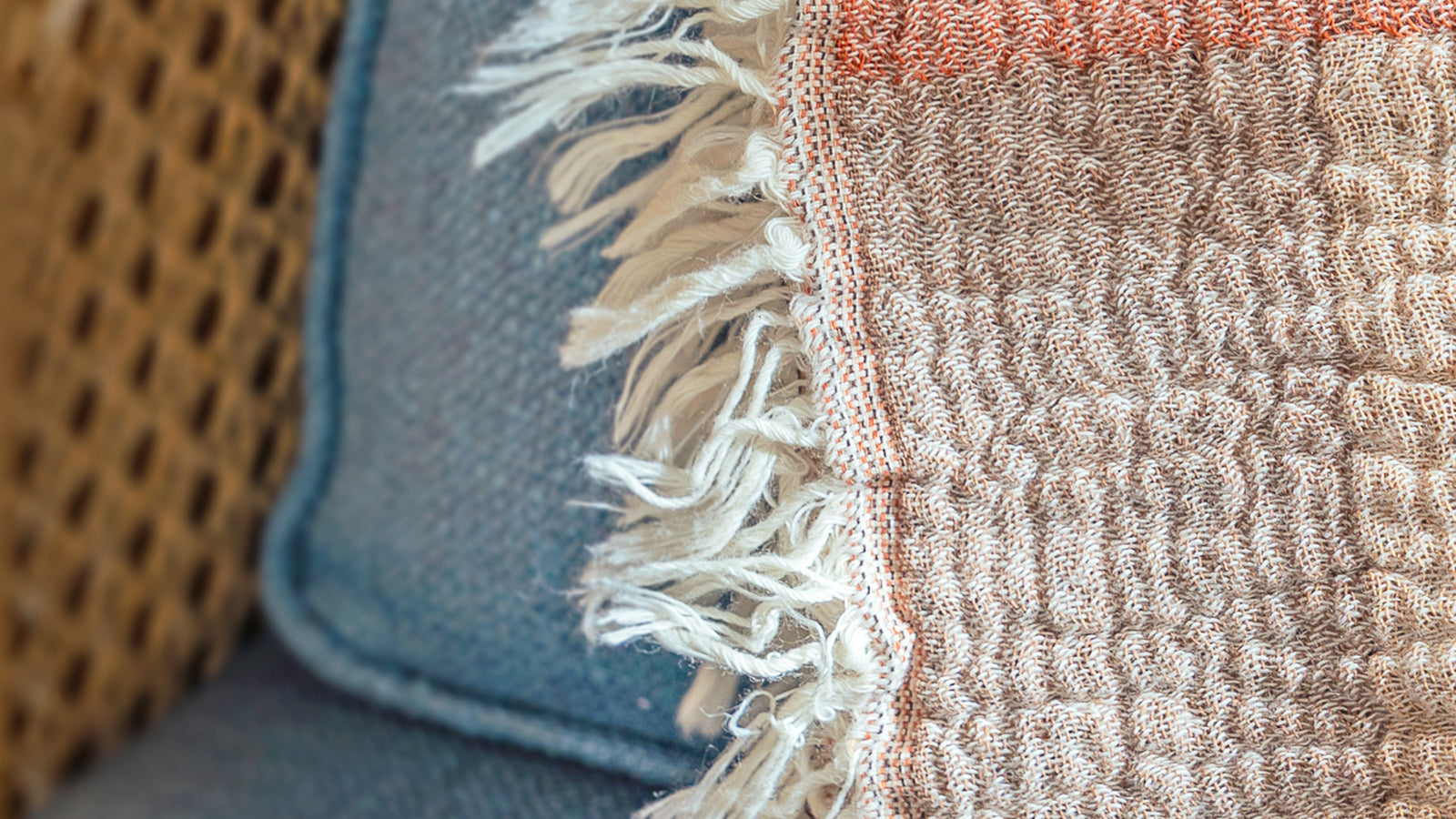 Close-up of textured fabric with frayed edge and a cushion in the background