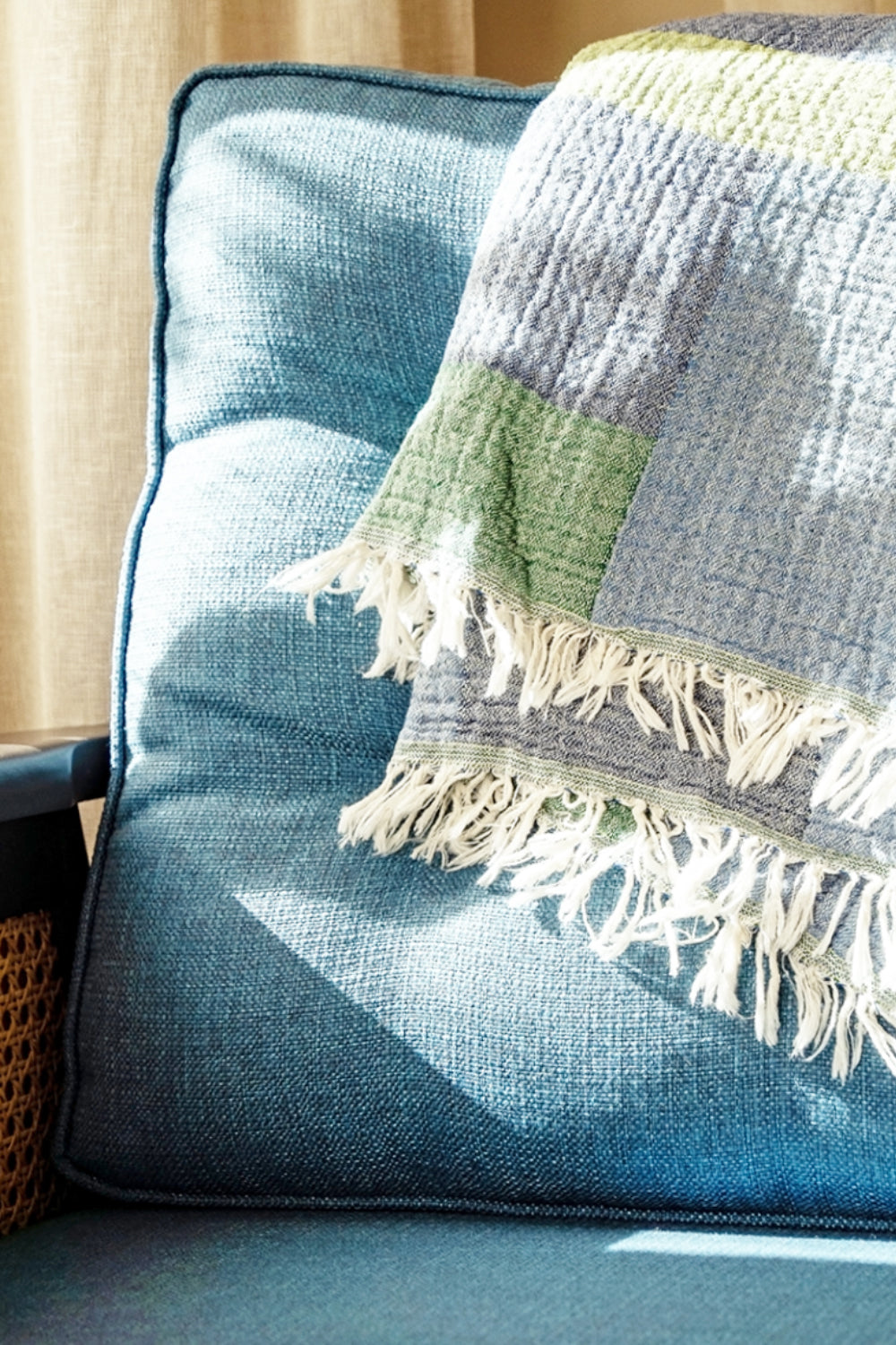 Textured blanket with fringes draped over a blue cushioned chair.