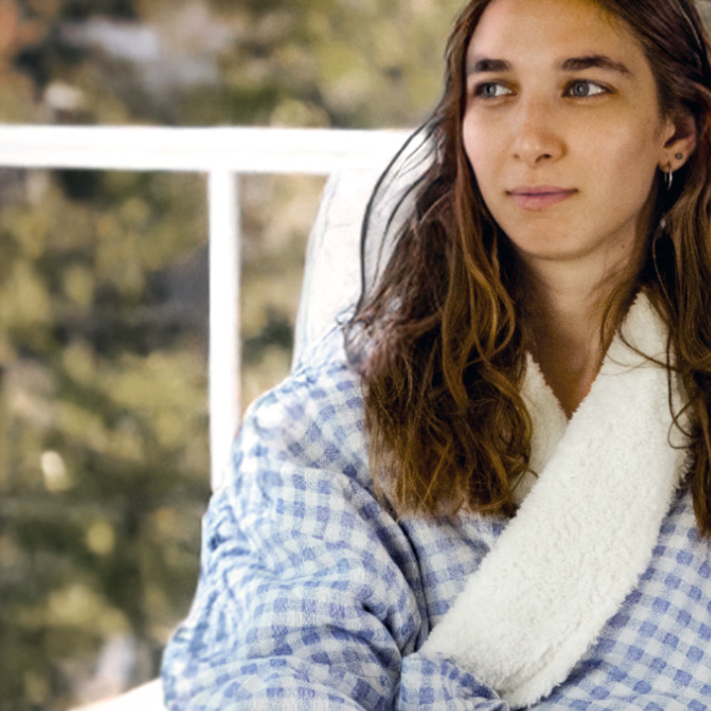 Woman wearing a blue checkered robe with white trim sitting outdoors.