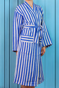 Young woman wearing a blue and white striped robe against a blue background