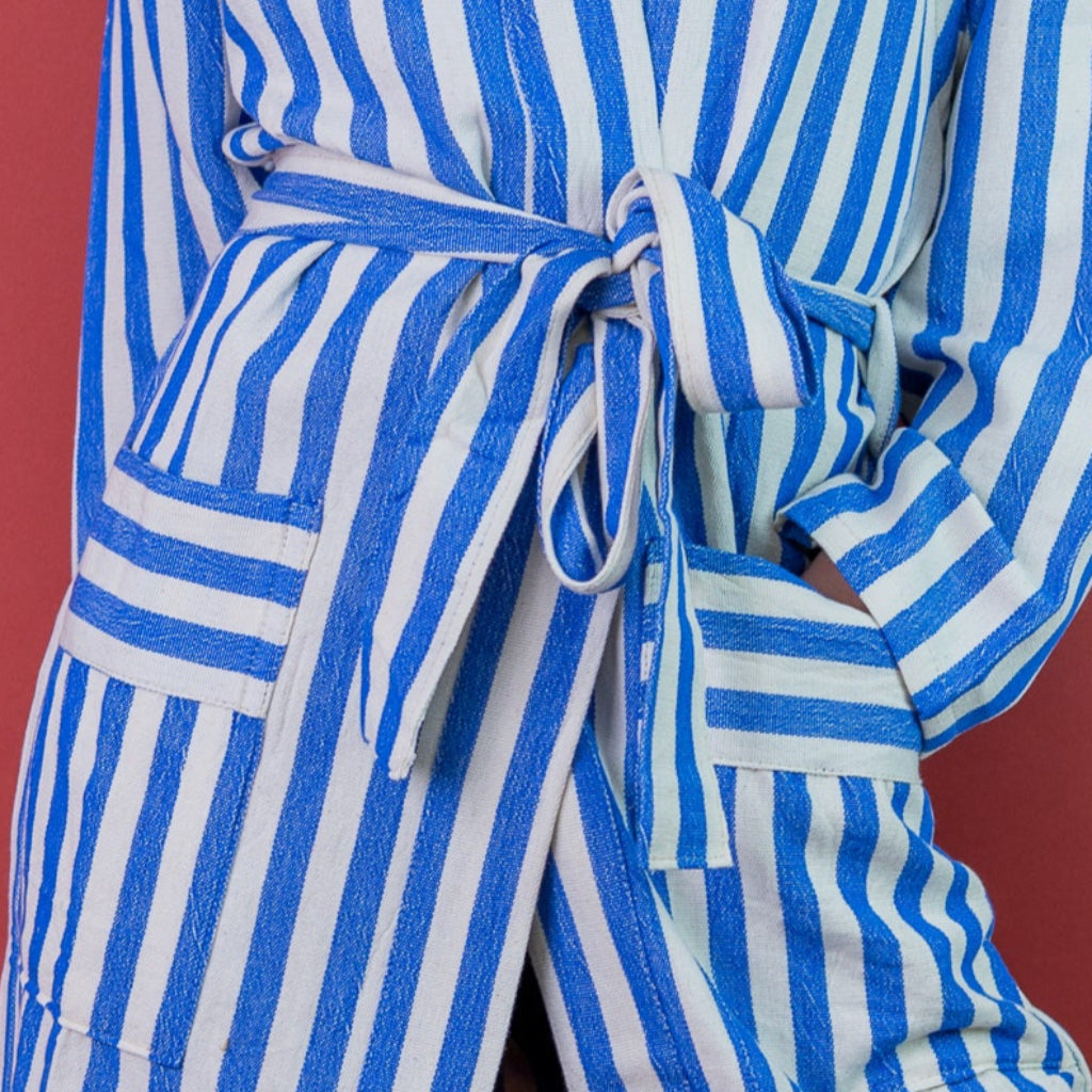 Young woman wearing a blue and white striped robe against a blue background