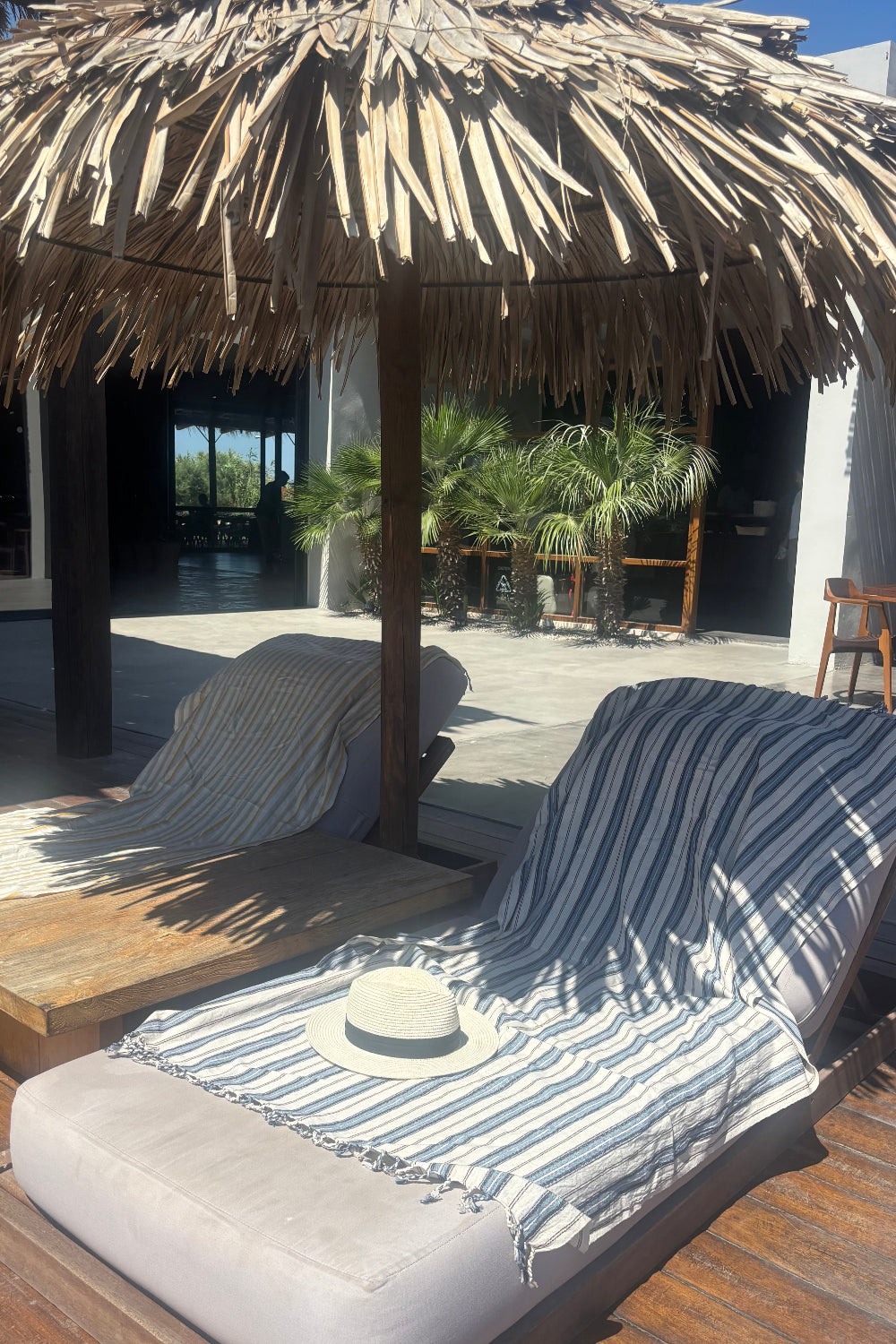 Outdoor setting with a thatched roof structure and striped cushioned chair.