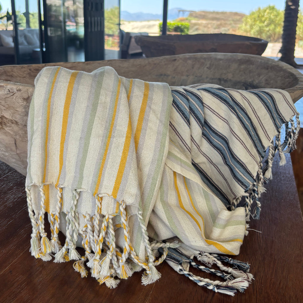 Striped Turkish towels with tassels on a wooden surface and in a wooden bowl, outdoor setting