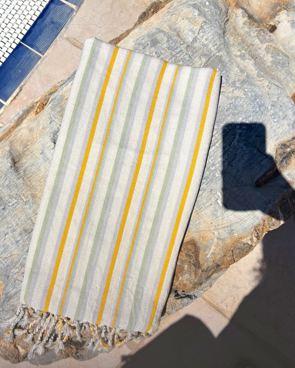 Striped Turkish peshtemal towel with yellow and gray stripes on a stone surface