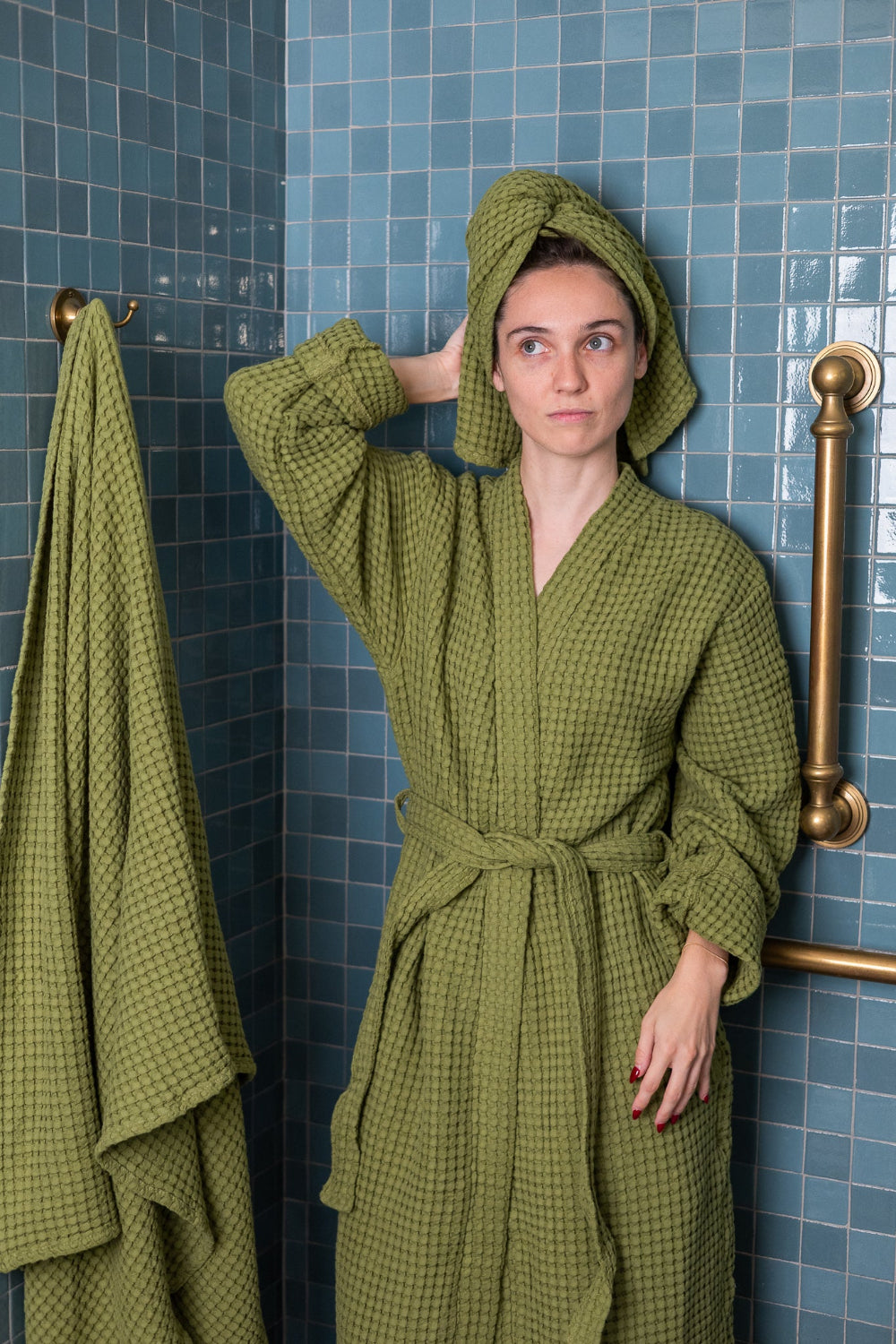 Woman wearing a green checkered robe and towel in a bathroom with blue tiles.
