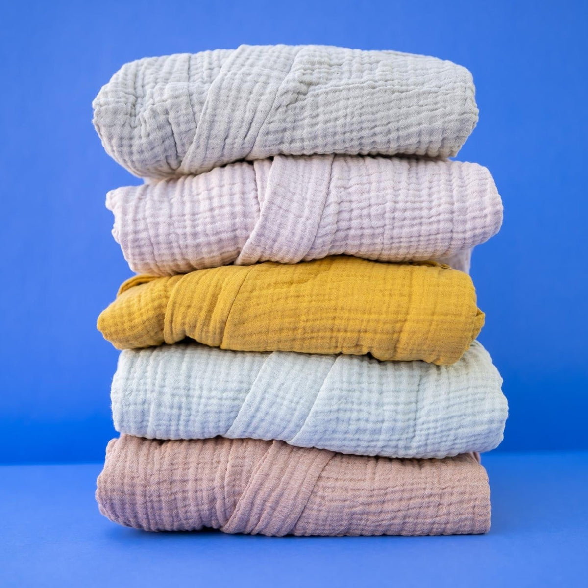 A stack of folded spa bathrobes in various solid colors including blue, pink, yellow, and green, displayed against a blue background.