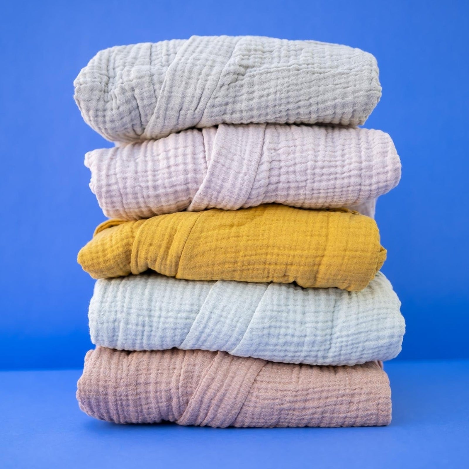 A stack of folded spa bathrobes in various solid colors including blue, pink, yellow, and green, displayed against a blue background.