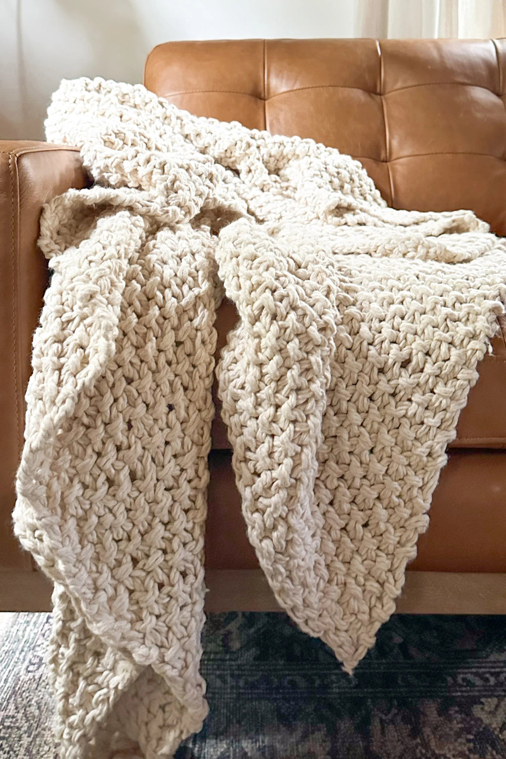 Beige knitted blanket draped over a brown leather sofa in a living room.