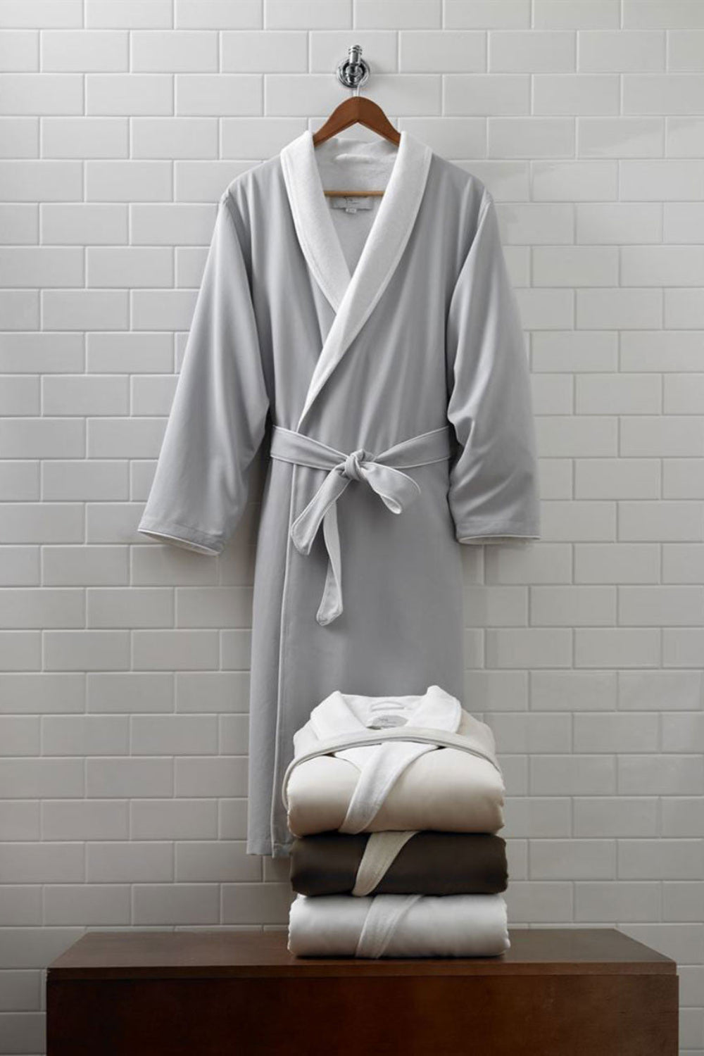 Gray bathrobe and folded towels on a wooden surface against a tiled wall.