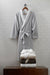Gray bathrobe and folded towels on a wooden surface against a tiled wall.