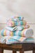Stack of colorful towels on a wooden stool against a white wall