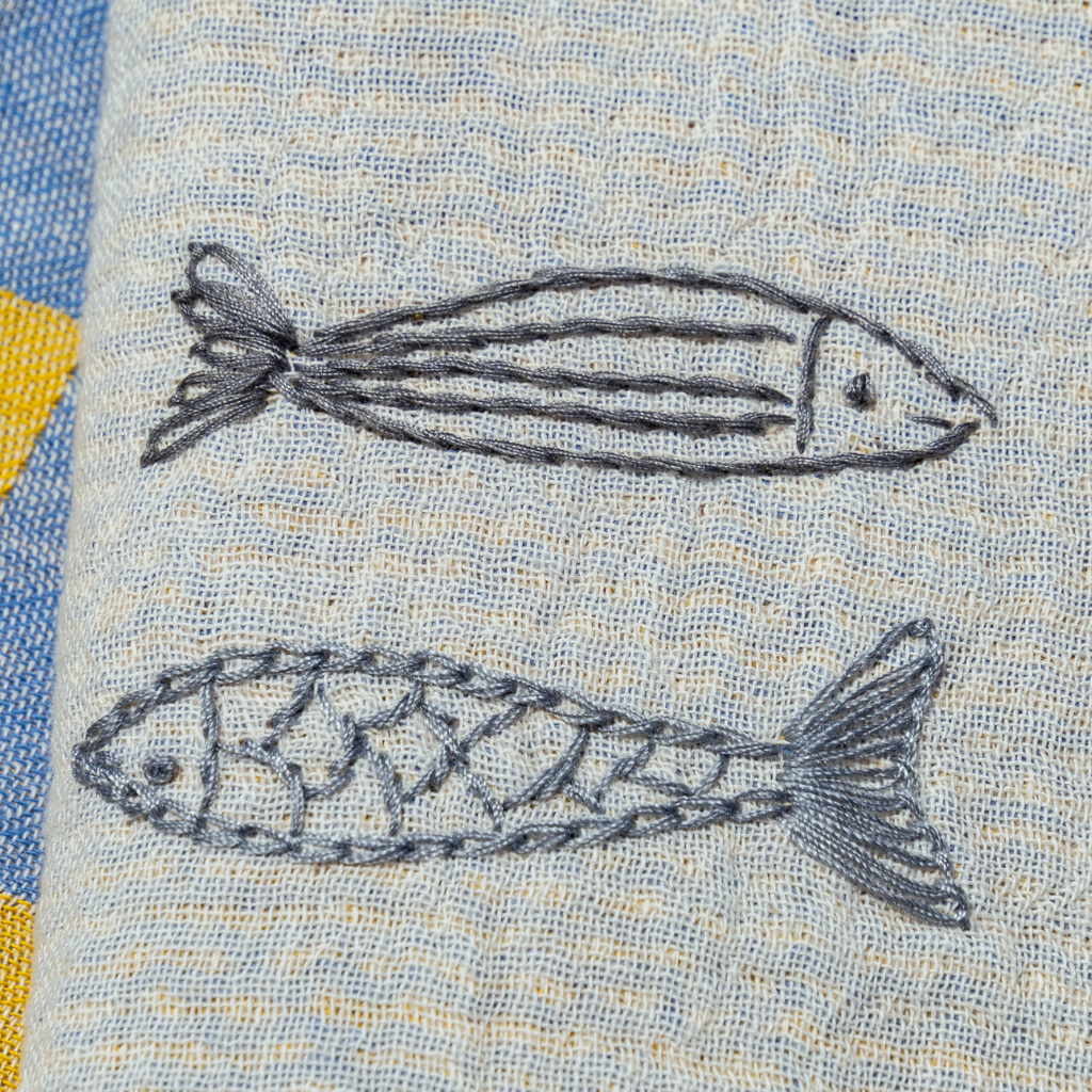 Two embroidered fish on a textured fabric background