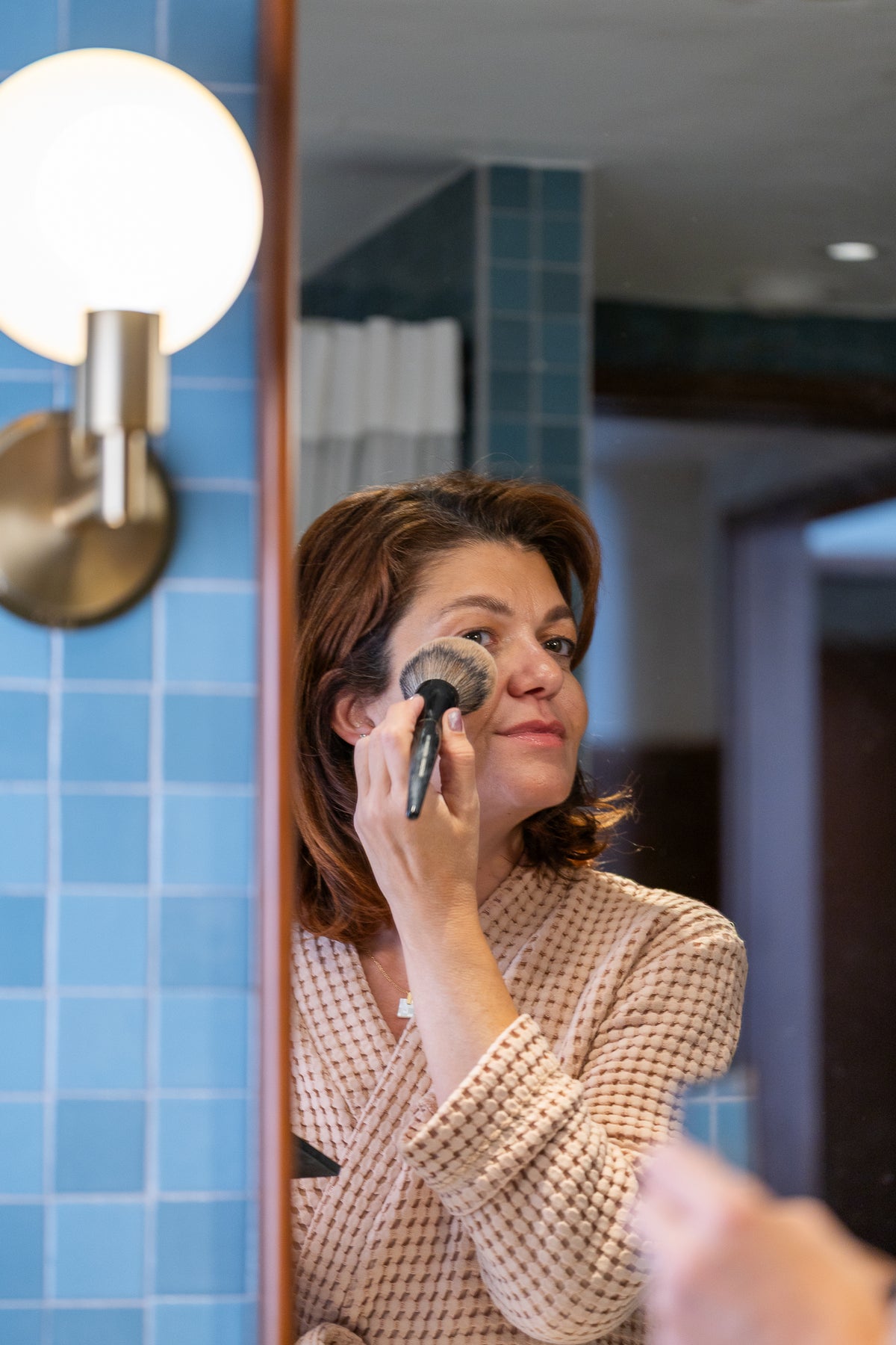 Woman wearing a sienna waffle robe applying makeup in front of a bathroom mirror