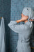 Person in a blue waffle bathrobe with a towel on their head in a bathroom with blue tiles.