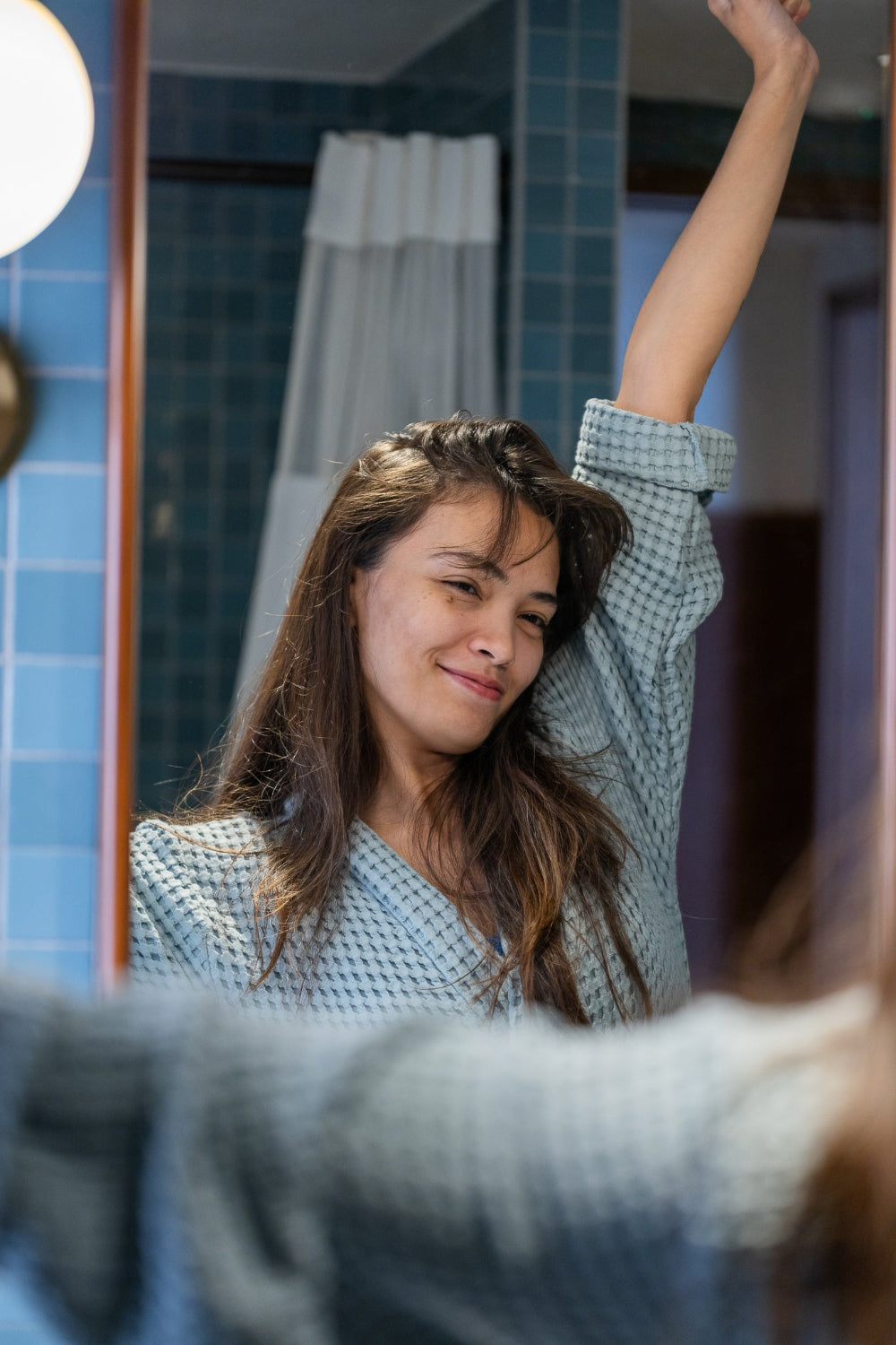 Woman stretching in front of a mirror and blue tiles wearing a blue waffle bathroom.