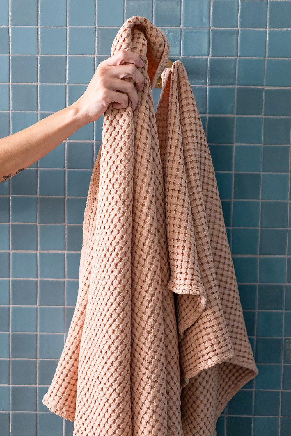 Person holding a beige towel against a blue tiled wall