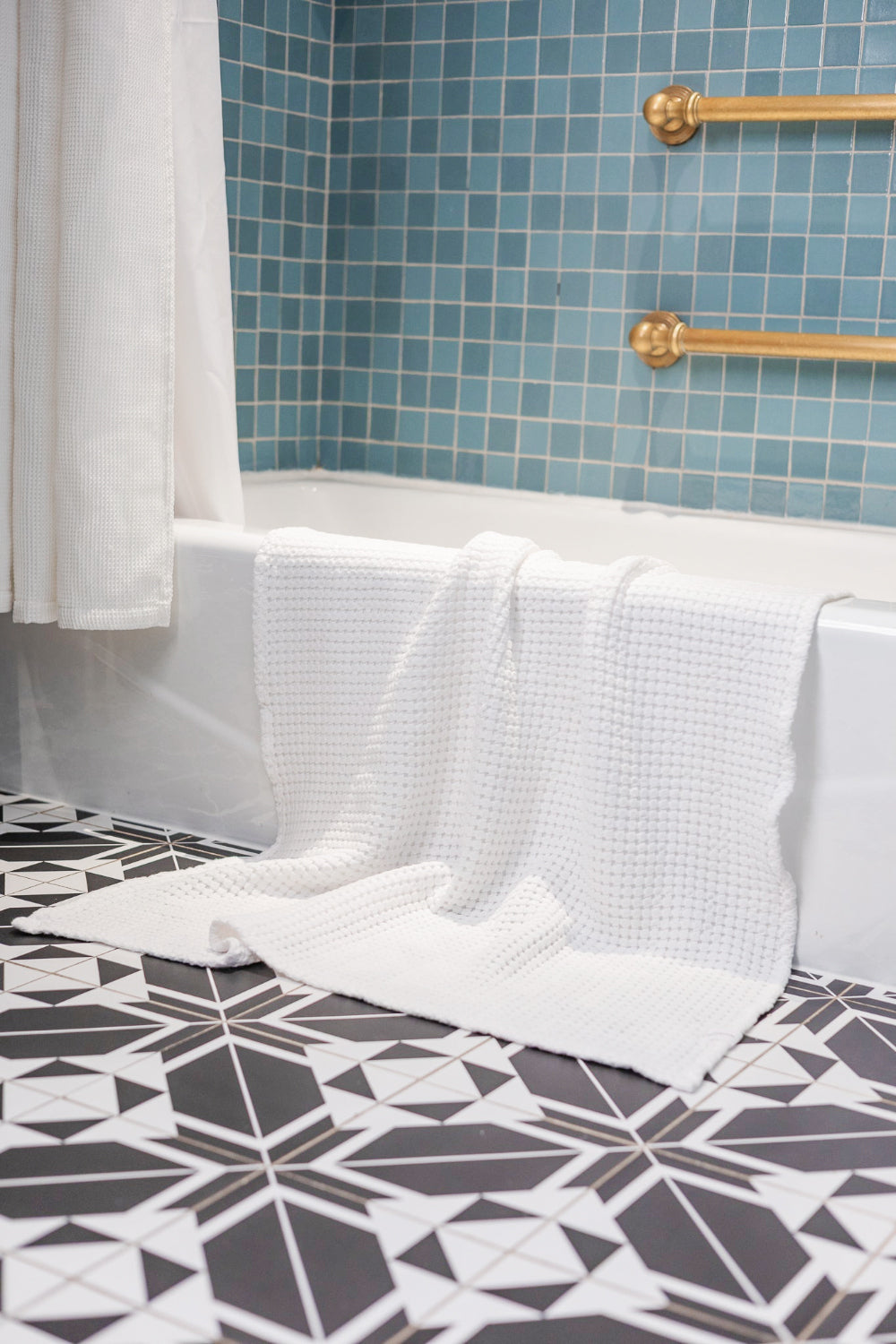 Bathroom with white bathtub, towels, and blue tiled wall.