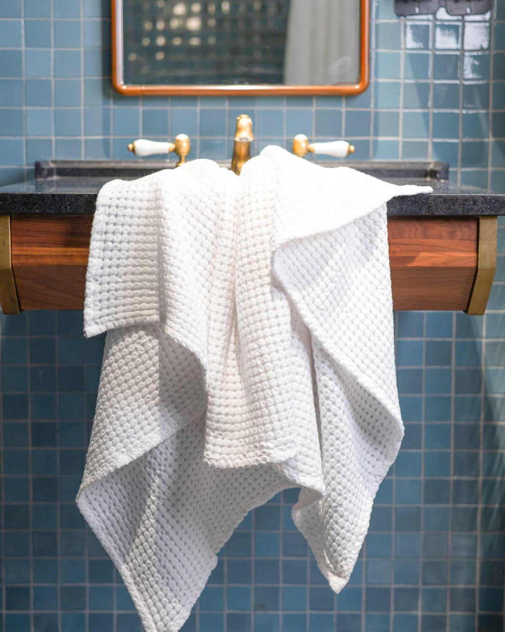 Bathroom with blue tiled walls, wooden vanity, and white towel.