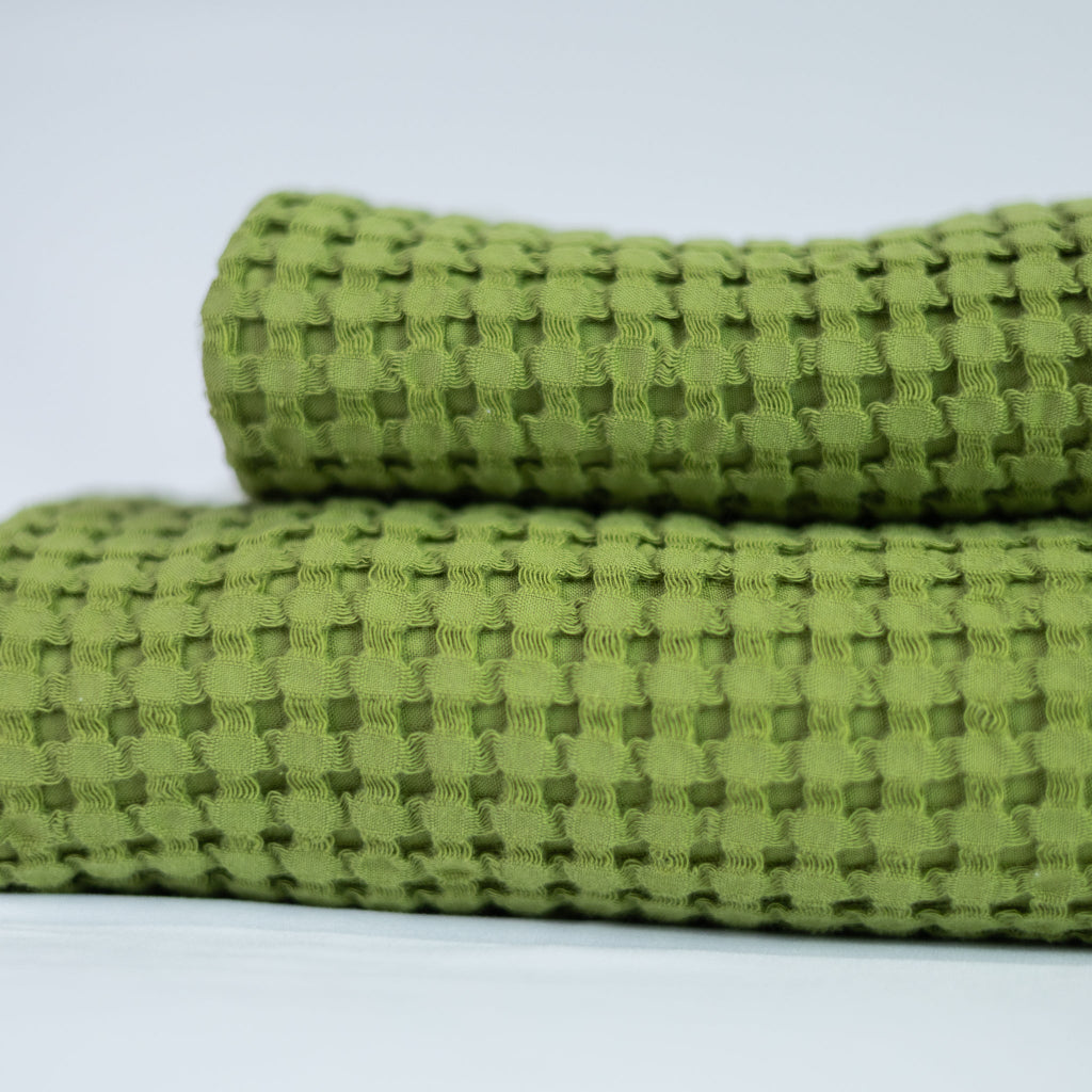 Two folded textured olive green towels on a light grey background