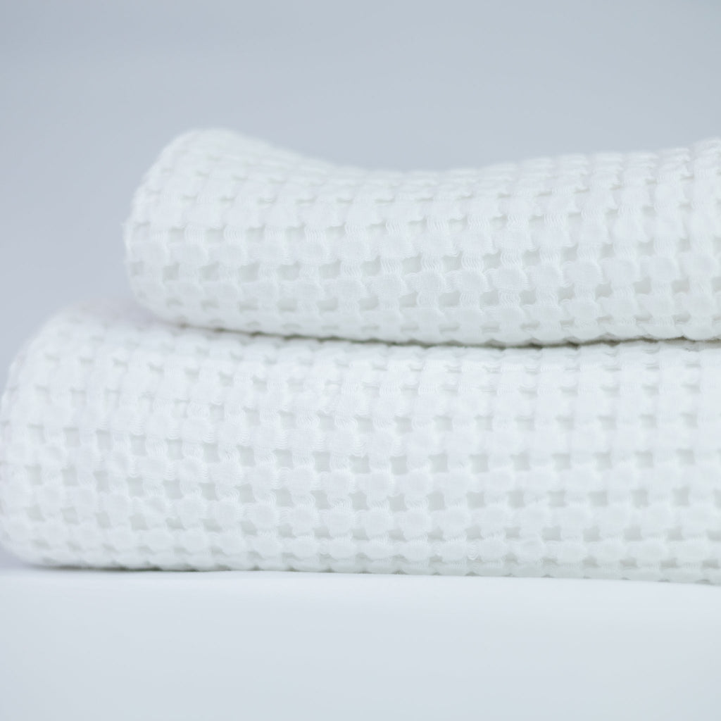 Two folded textured white towels on a light grey background