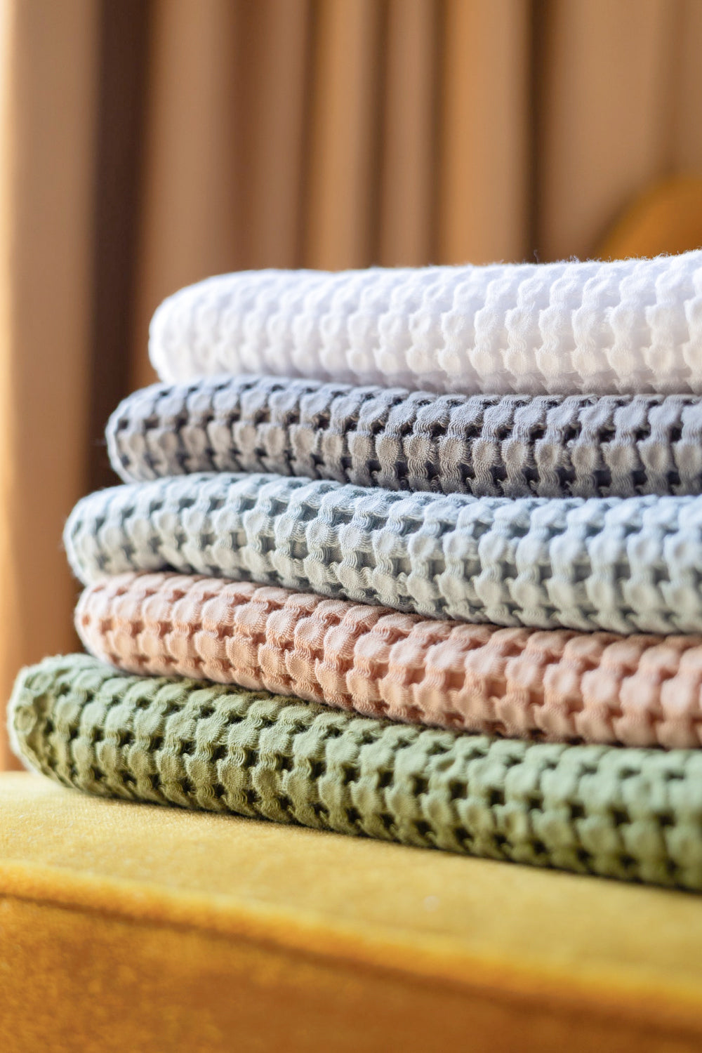Stack of colorful textured towels on a yellow chair with a blurred background